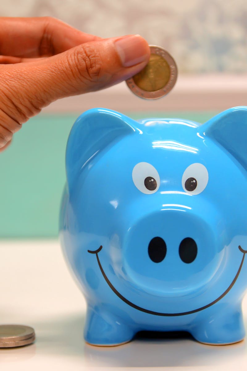 Hand inserting a coin into a blue piggy bank for savings and money management.